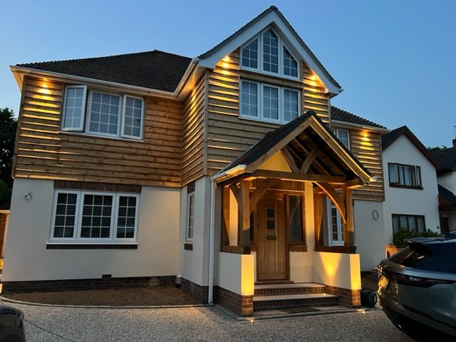 A modern two-toned house with wooden cladding and an illuminated entrance.