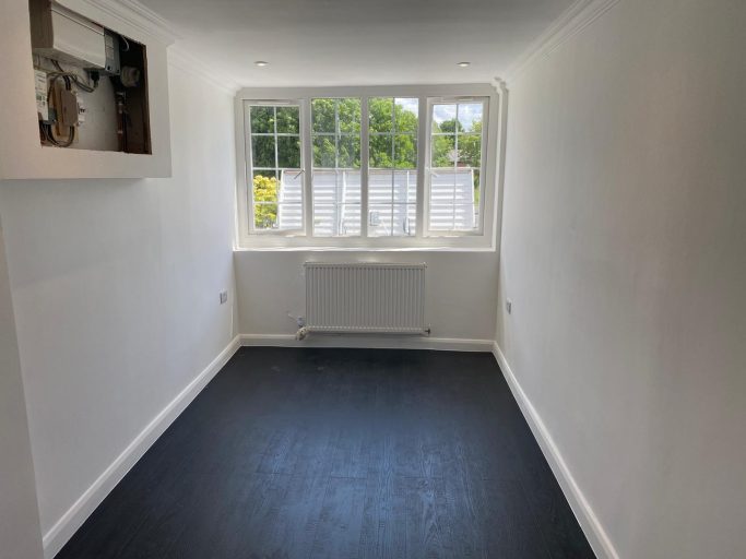 Empty room with white walls, a window, and dark flooring.