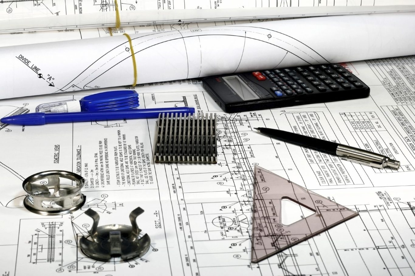 Technical drawing materials including a calculator, pens, and drafting tools on blueprints.