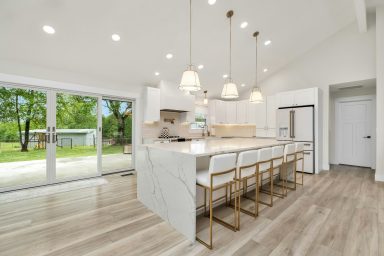 Modern kitchen with white marble countertops, gold accents, and a view of the outdoors.