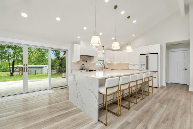 Modern kitchen with marble countertops, stylish bar stools, and large sliding doors to a garden.