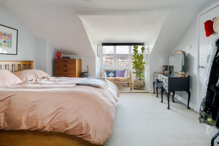 Bright attic bedroom with a pink duvet, a mirror, and large windows overlooking a patio.