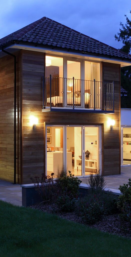 Modern two-storey house with wooden facade, lit windows, and evening sky.