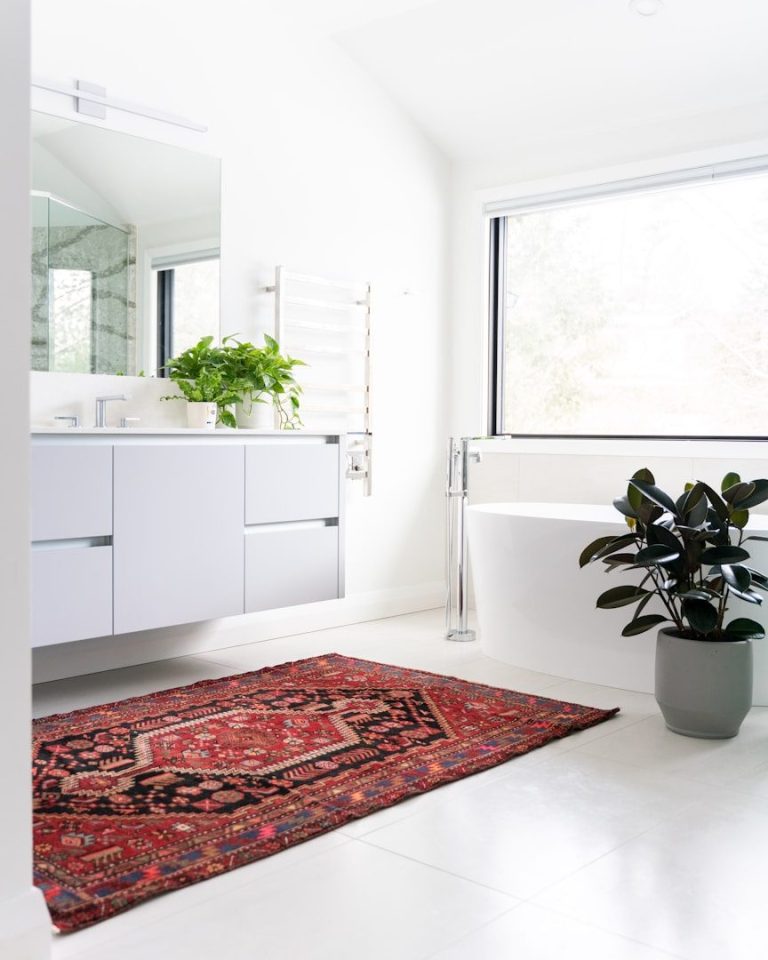A modern bathroom featuring a white bathtub, sink, and a red patterned rug.