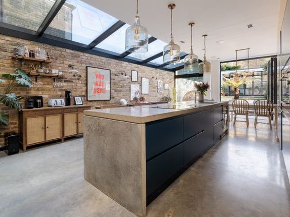 Modern kitchen with a concrete island, wooden furniture, and large glass windows.