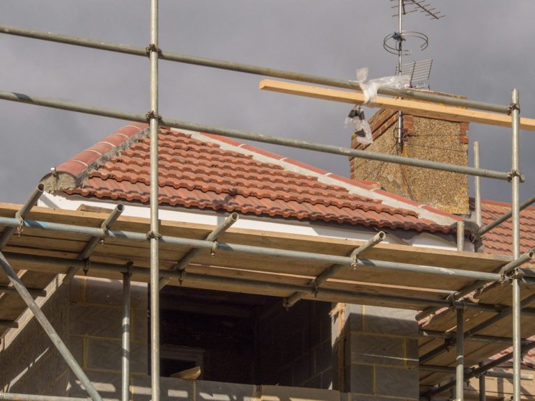 Roof with red tiles under construction, supported by scaffolding.