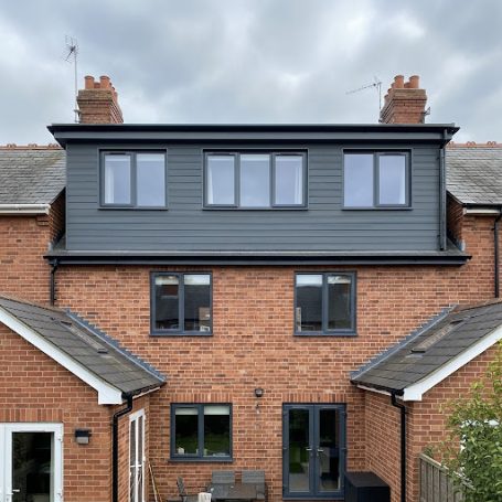 Modern brick house with a dark grey upper extension and several windows.